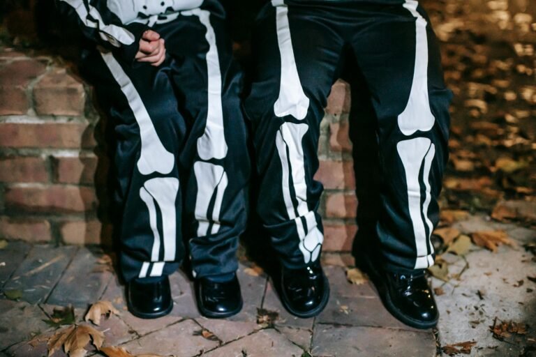 Crop faceless kids in skeleton costumes sitting on brick bench